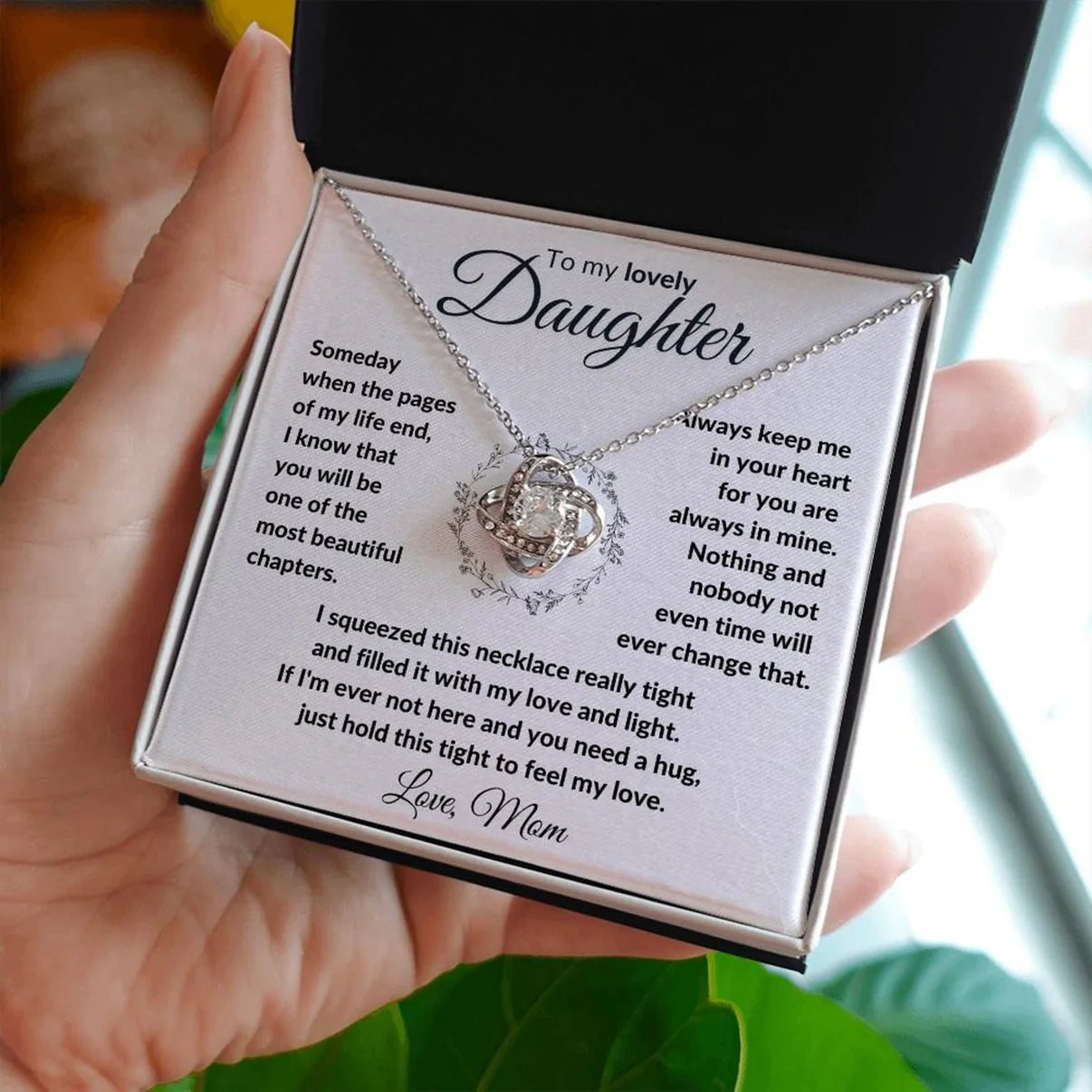 A hand holding a LED lighted gift box with a necklace inside, intended as a gift from a mother to her daughter, featuring a message card.